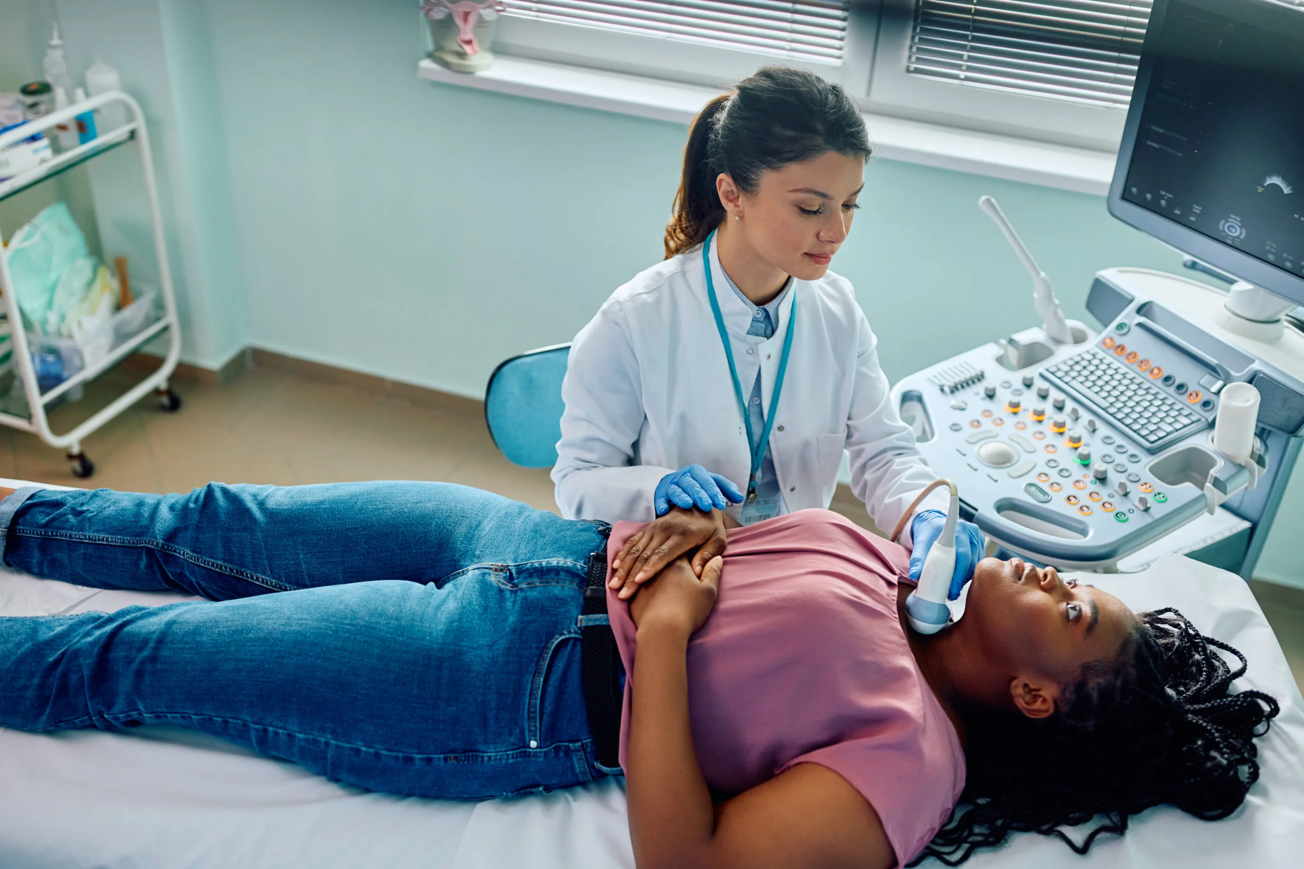 Female doctor using ultrasound while examining black woman's neck at medical clinic.